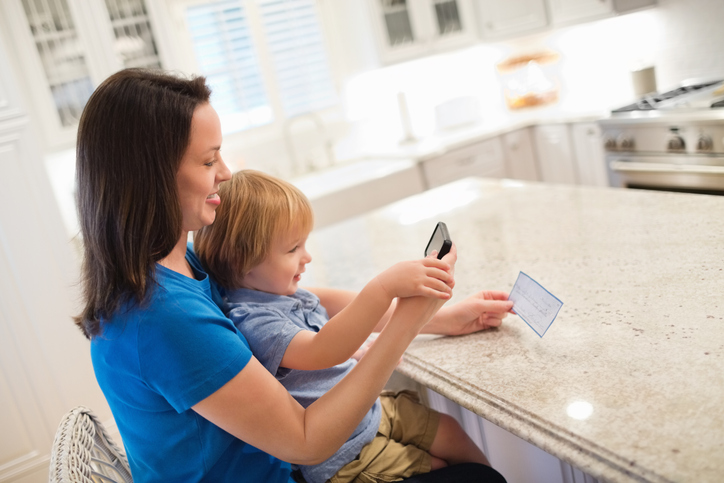 Mother And Son Depositing Check Through Smart Phone Bank Landing Image